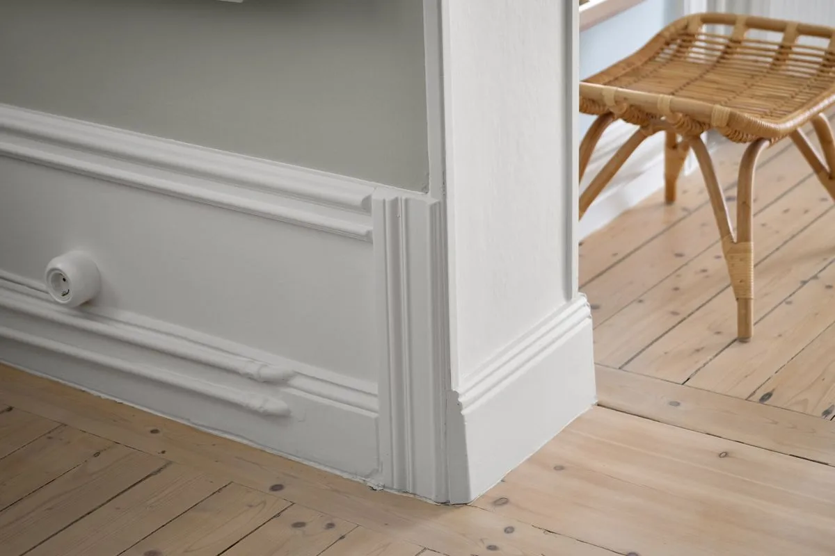 White profiled baseboard meeting a door casing above a pale wood floor